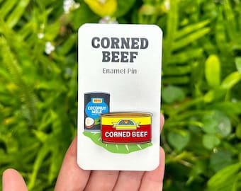 May include: A white card with the text "CORNED BEEF Enamel Pin" and an illustration of a can of corned beef and a can of coconut milk.