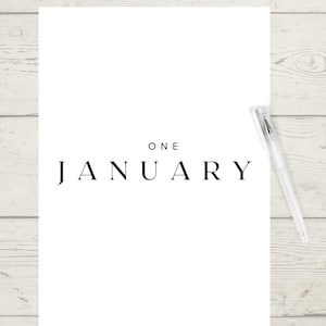 May include: A white sheet of paper with the words "ONE JANUARY" in black, stylish font. A clear pen is positioned on the right side. The background features a light wood grain.