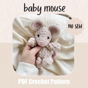 May include: A crocheted baby mouse in light pink with pink inner ears and a pink tail. The mouse is held in a hand. The image includes the text "baby mouse", "NO SEW", and "PDF Crochet Pattern".