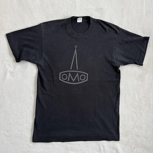 May include: Black t-shirt with a gray graphic design. The design features a stylized tower shape above the letters "OMO" inside a hexagon. The shirt is made of a soft material and has a crew neck.
