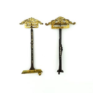 Peut inclure: Deux supports en métal doré antique avec des motifs de volutes ornés. Les supports sont fixés à des tiges en métal noir.
