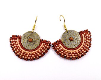 May include: A pair of earrings with a fan-shaped design made of brown, beige and black beads. Each earring features a round, textured, brass-coloured metal piece in the centre.
