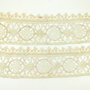 以下が含まれることがあります： 小さな円と複雑なデザインが繰り返されるパターンを持つ、繊細なオフホワイトのレーストリムが2つ。レースは手作りで、ヴィンテージな外観です。