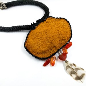 May include: A brown felt pendant necklace with black beads, orange stones, and a feather accent.