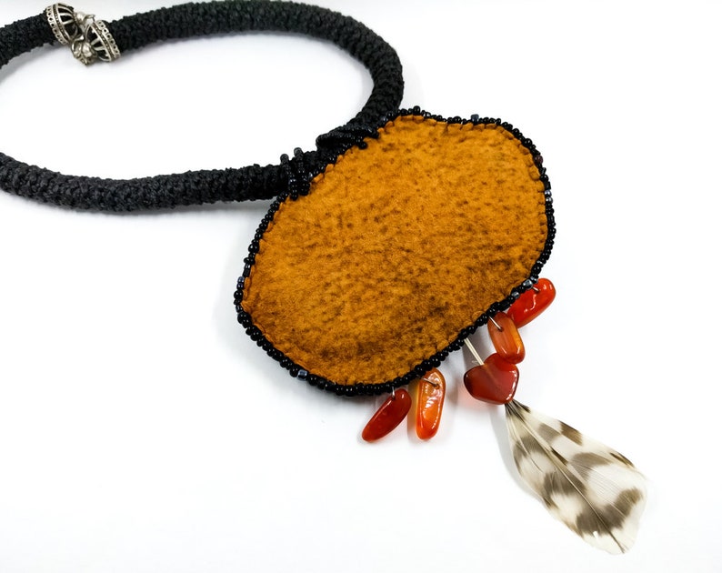 May include: A brown felt pendant necklace with black beads, orange stones, and a feather accent.