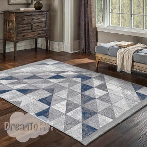 May include: A grey and blue geometric area rug with a pattern of triangles. The rug has a light grey border.