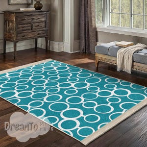 May include: A teal and white area rug with a geometric pattern of overlapping circles. The rug has a cream-coloured border.
