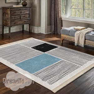 May include: Abstract geometric rug with black, white, and blue stripes and squares. The rug has a cream-colored background and a white border.