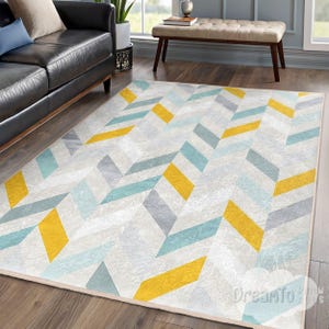 May include: A rectangular area rug with a geometric chevron pattern. The rug features a light gray background with yellow, teal, and gray geometric shapes. The rug is placed on a hardwood floor.