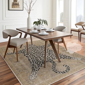 May include: A dining room scene featuring a rectangular wooden table with four chairs. A beige rug with a large leopard print design is beneath the table. White vases and tableware are on the table. A framed picture hangs on the wall.
