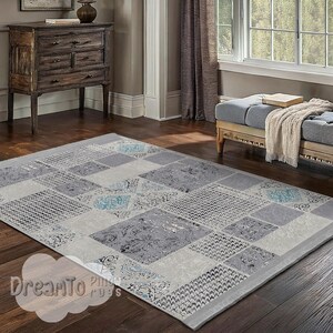 May include: A gray and white patterned area rug with a geometric design. The rug has a subtle blue and teal color throughout the pattern. The rug is laid out on a hardwood floor in a living room setting.