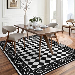 Op de afbeelding: Een zwart-wit geblokt tapijt met een decoratieve zwarte rand met een swirl-patroon. Het tapijt ligt onder een houten eettafel met twee stoelen.