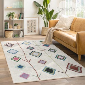 Puede incluir: Una alfombra blanca con un patrón geométrico de cuadrados coloridos y ramas. La alfombra tiene un fondo crema con ramas marrones y cuadrados multicolores.