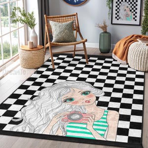 May include: A black and white checkered area rug featuring a cartoon illustration of a girl with long white hair holding a pink camera. The girl is wearing a green and white striped top. The rug has a black border.
