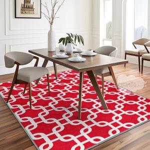 Może przedstawiać: Geometryczny dywan w kolorze czerwonym i białym z powtarzającym się wzorem splecionych kół. Dywan znajduje się pod drewnianym stołem jadalnym z dwoma krzesłami.