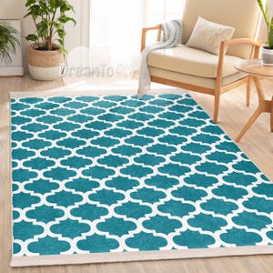 Könnte beinhalten: Teppich in Teal und Weiß mit geometrischem Muster. Der Teppich hat einen weißen Rand und liegt auf einem Holzboden.