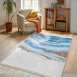 May include: A white and blue abstract area rug with a modern design. The rug features a white background with blue and gold abstract lines.