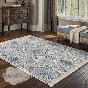 May include: A blue and gray patterned area rug with a cream border. The rug is laid out on a hardwood floor in a living room setting.