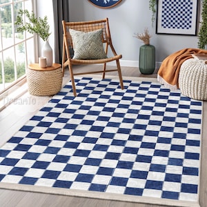 Op de afbeelding: Een blauw-wit geblokt tapijt met een witte rand. Het tapijt ligt op een houten vloer in een woonkamer.