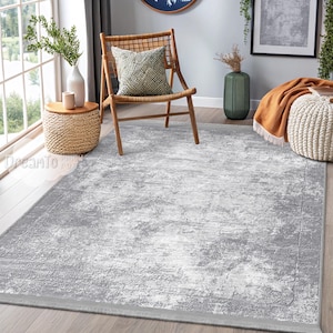 Puede incluir: Una alfombra gris y blanca desgastada con un patrón sutil. La alfombra está colocada sobre un suelo de madera en un salón con una silla y una mesa auxiliar.