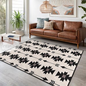 Puede incluir: Alfombra rectangular con un fondo crema y un patrón repetido de formas geométricas negras y grises que se asemejan a flechas. La alfombra está colocada en un salón con un sofá de cuero marrón y una mesa de centro.