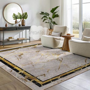 May include: A beige and gold area rug with a marble pattern and black and gold border. The rug is in a living room setting with two white chairs and a wooden side table.
