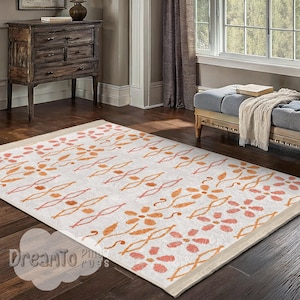 May include: A rectangular area rug with a cream-colored background and an orange and pink floral pattern. The rug has a beige border and is placed on a dark wood floor. The rug is in a living room setting.