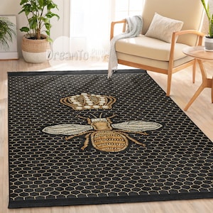 Può includere: Tappeto da area nero e oro con un motivo a nido d'ape e un'ape con una corona in testa.