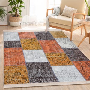 Könnte beinhalten: Ein Patchwork-Teppich mit verschiedenen Farben und Mustern, darunter Orange, Gelb, Grau und Weiß. Der Teppich hat einen abgenutzten Look, der ihm ein Vintage-Feeling verleiht.