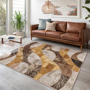 May include: A brown, beige and gold area rug with a geometric pattern of curved lines and squares. The rug is in a living room with a brown leather sofa and a potted plant.