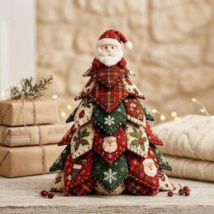 May include: A decorative fabric Christmas tree ornament featuring a plush Santa Claus topper. The tree is constructed from layered, quilted fabric triangles in red and green, decorated with patterns of Santa faces, snowflakes, holly leaves, and stockings.