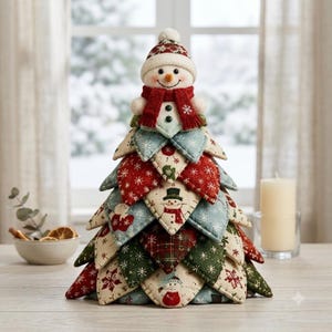 Può includere: Un ornamento decorativo per albero di Natale in tessuto con un design trapuntato a strati e vari motivi natalizi, inclusi fiocchi di neve e pupazzi di neve. Una figura di pupazzo di neve in peluche con sciarpa e cappello rossi si trova in cima.