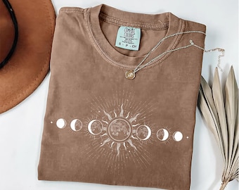 Op de afbeelding: Een bruin t-shirt met een witte afbeelding van een zon en maanfasen. Het shirt heeft de tekst "Comfort Colors" en "S-P-CH" op de voorkant.