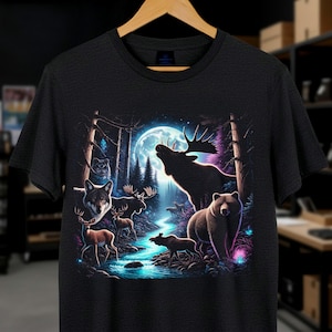 May include: Black t-shirt featuring a vibrant forest scene with a full moon, a flowing river, and various wildlife. The design includes a wolf, moose, bear, and deer, creating a nature-themed graphic.