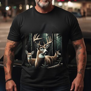 Puede incluir: Una camiseta negra de manga corta con un estampado gr&aacute;fico de tres ciervos en un bosque oscuro. El ciervo central tiene astas grandes, mientras que los otros dos est&aacute;n situados a los lados. El dise&ntilde;o utiliza tonos naturales marrones y blancos.