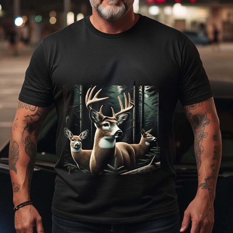 Puede incluir: Una camiseta negra de manga corta con un estampado gr&aacute;fico de tres ciervos en un bosque oscuro. El ciervo central tiene astas grandes, mientras que los otros dos est&aacute;n situados a los lados. El dise&ntilde;o utiliza tonos naturales marrones y blancos.