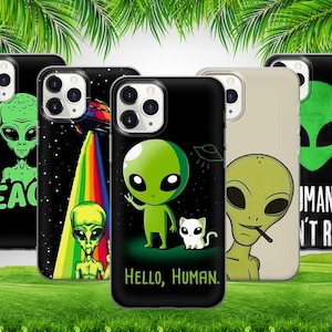 May include: Four different phone cases featuring alien designs. The first case is black with a green alien holding a peace sign and the text "Peace". The second case is black with a rainbow and a green alien. The third case is black with a green alien holding a peace sign and the text "Hello, Human". The fourth case is beige with a green alien smoking a cigarette and the text "Humans aren't real".