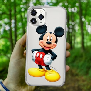 May include: A clear phone case with a Mickey Mouse design. Mickey Mouse is wearing red shorts with two black buttons and yellow shoes. Mickey Mouse is standing with his hands on his hips and smiling.