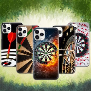 May include: A collection of phone cases featuring dartboard designs. The cases display various dartboard themes, including a dart with a red flight, a dart hitting the board, and a board engulfed in flames. The cases have a glossy finish.