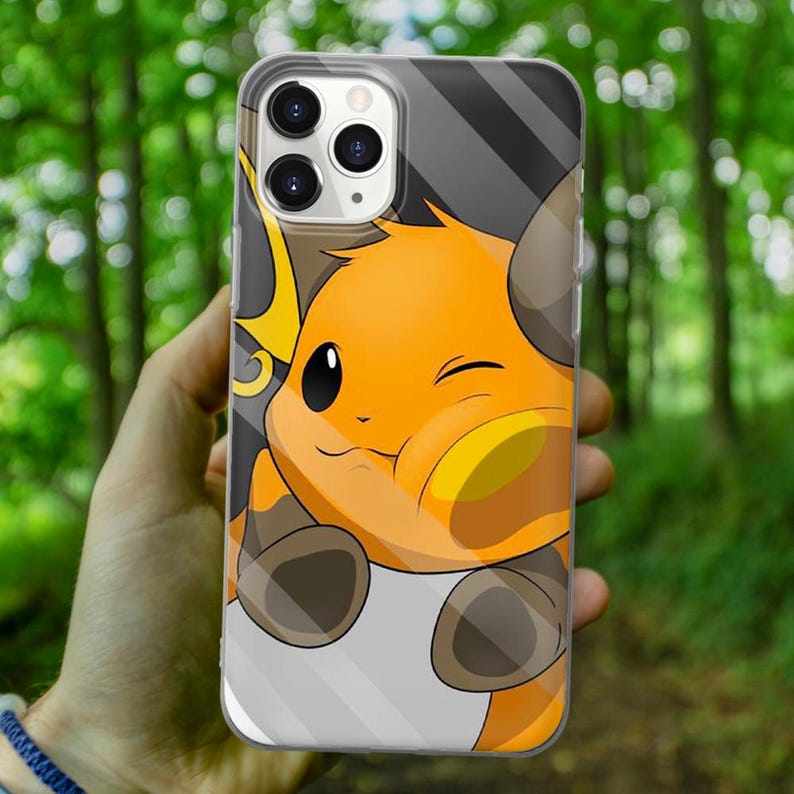 May include: A clear phone case with a cartoon image of a yellow and orange Pokemon character with brown fur and a winking eye. The character is holding its paw up to its face.