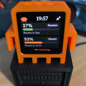 Könnte beinhalten: Ein orangefarbenes, roboterförmiges digitales Anzeigegerät mit schwarzem Sockel. Der Bildschirm zeigt die Uhrzeit 19:57, einen 27%-Sitzungsfortschrittsbalken, einen 53%-Wochenfortschrittsbalken und den Text Marinating an.