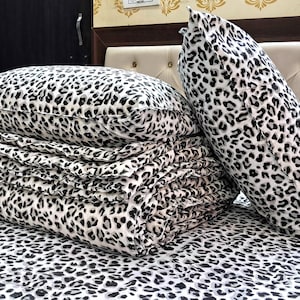 May include: A bed set featuring a black and white leopard print pattern. The set includes a folded blanket, two pillows, and a fitted sheet. The pillows are rectangular and cylindrical. The bedding is neatly arranged on a bed.