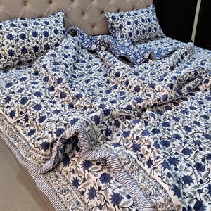 May include: A white and blue floral patterned quilt set with two matching pillowcases. The quilt is made of cotton and has a hand-stitched design.