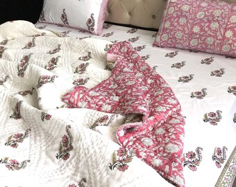May include: A bed is made with a white quilt and matching pillowcases, all adorned with a floral pattern in pink and green. The bedspread has a pink floral design. The headboard is beige with a button-tufted design.