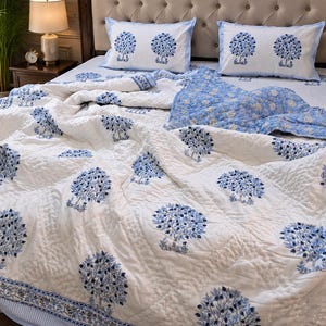 May include: A white quilted bedspread and two matching pillowcases featuring a repeating blue tree pattern. The bedding set includes a blue and white floral patterned underside, visible where the quilt is folded back on the bed.