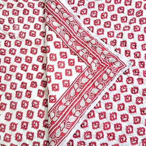 May include: A white and red floral patterned quilt. The quilt features a repeating pattern of red flowers on a white background. The border has a red stripe with a leaf design. The quilt is folded, showing the pattern and border details.