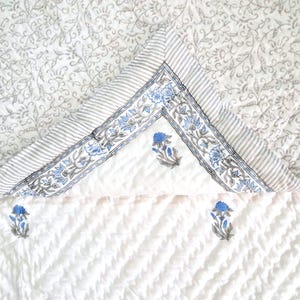May include: White cotton quilt with a blue and grey floral print. The quilt has a border of stripes and a floral pattern.