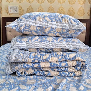May include: A blue and white floral patterned quilt set with a folded quilt and two matching pillowcases. The quilt is folded and stacked on top of the pillowcases.