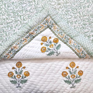 May include: White quilted bedspread with a floral design. The bedspread features a repeating pattern of green leaves and a border with yellow and green floral accents. The center has yellow floral bouquets.