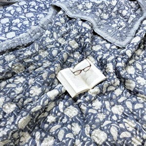 May include: A blue and white floral patterned quilt with a book and glasses on top.